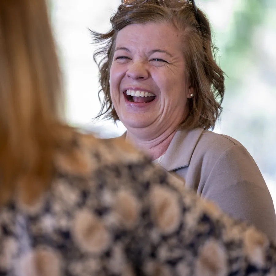 Two women engaged in a joyful conversation, one laughing heartily with natural light in the background.