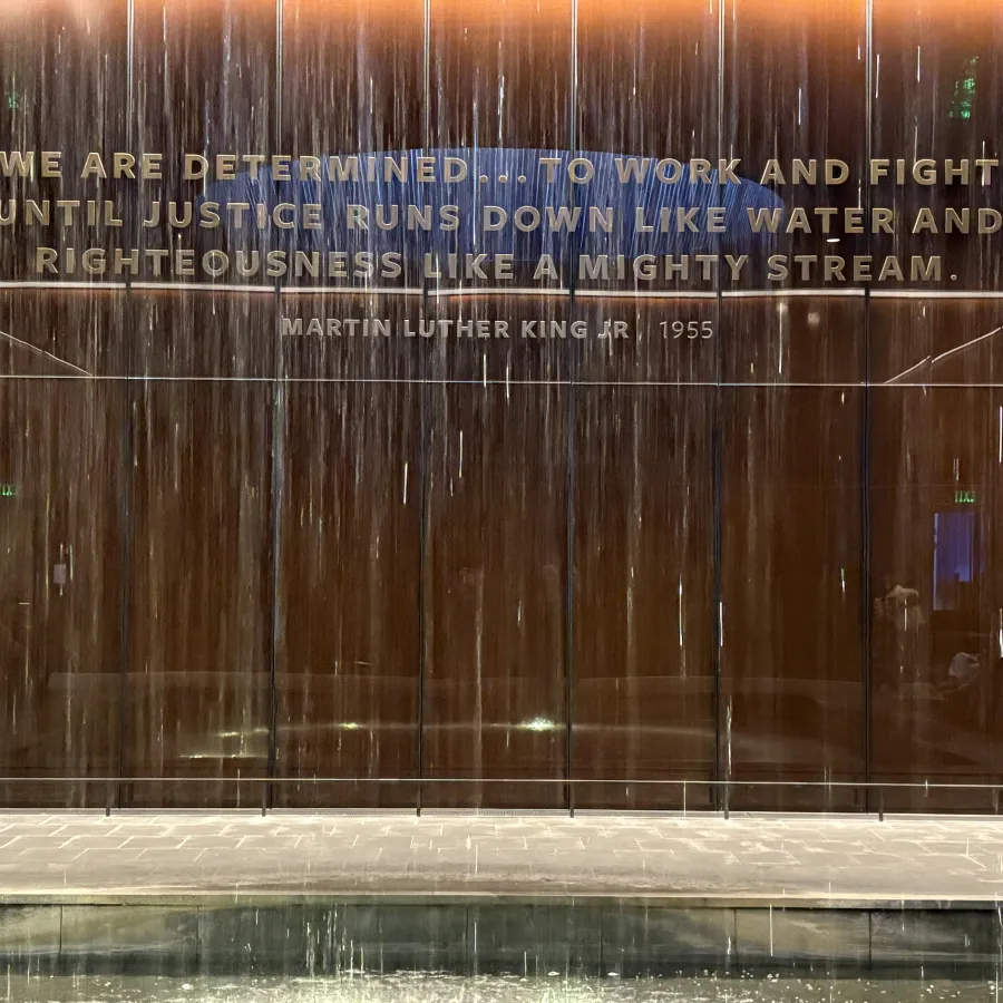 Waterfall feature with Martin Luther King Jr. 1955 quote on a bronze wall in a memorial setting at night.