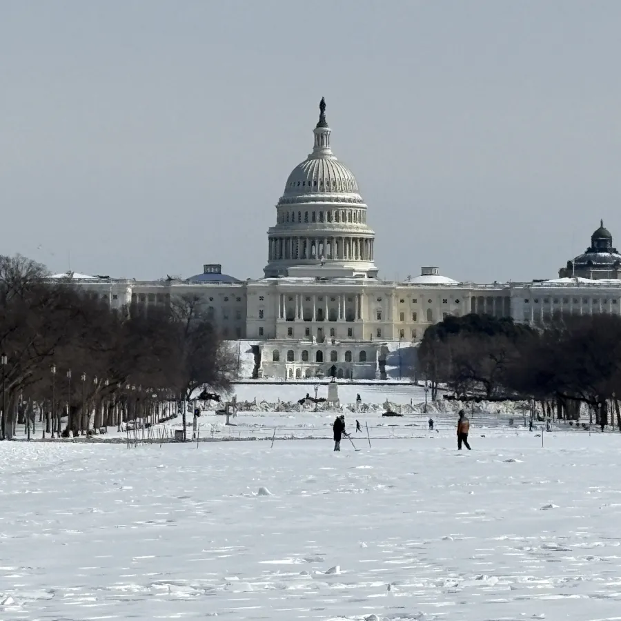 Snow-covered National Mall with the United States Capitol building in the background and people walking.