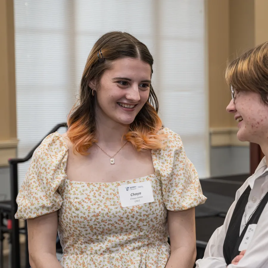 Two students smiling and chatting during an event at Berry College with name tags and podium in background.