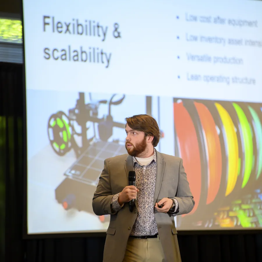 Man in suit giving presentation on flexibility and scalability with colorful filament spools and 3D printer image.