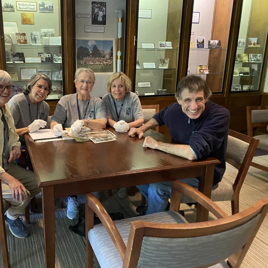 Five adults sitting around a wooden table in a museum room, reviewing historical documents with gloves and smiles.