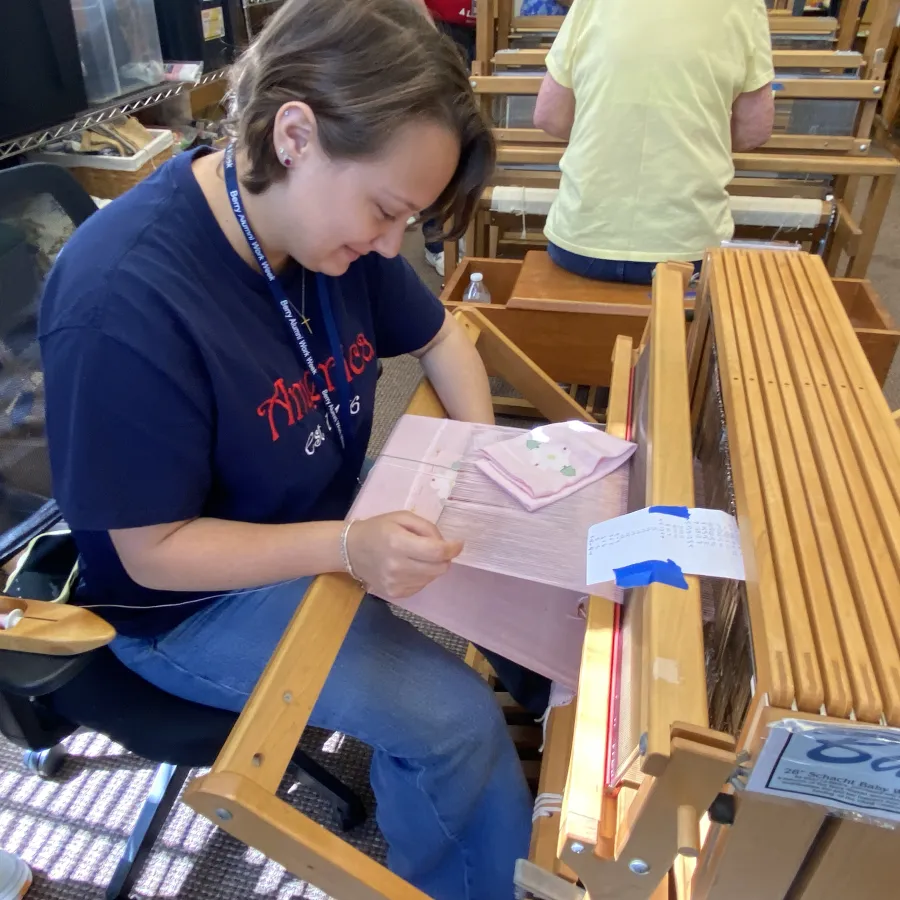 Woman weaving on a wooden loom in a workshop setting focused on textile creation.