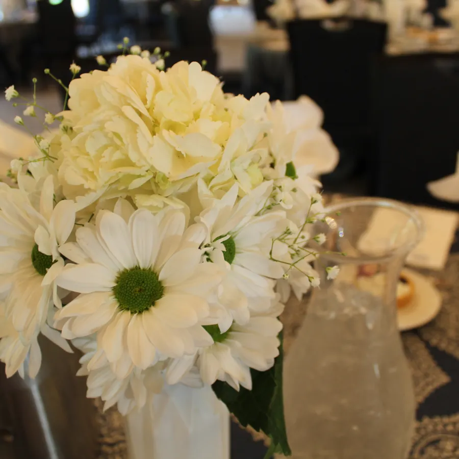 White daisies and hydrangeas arranged in a vase centerpiece on a decorated dining table.
