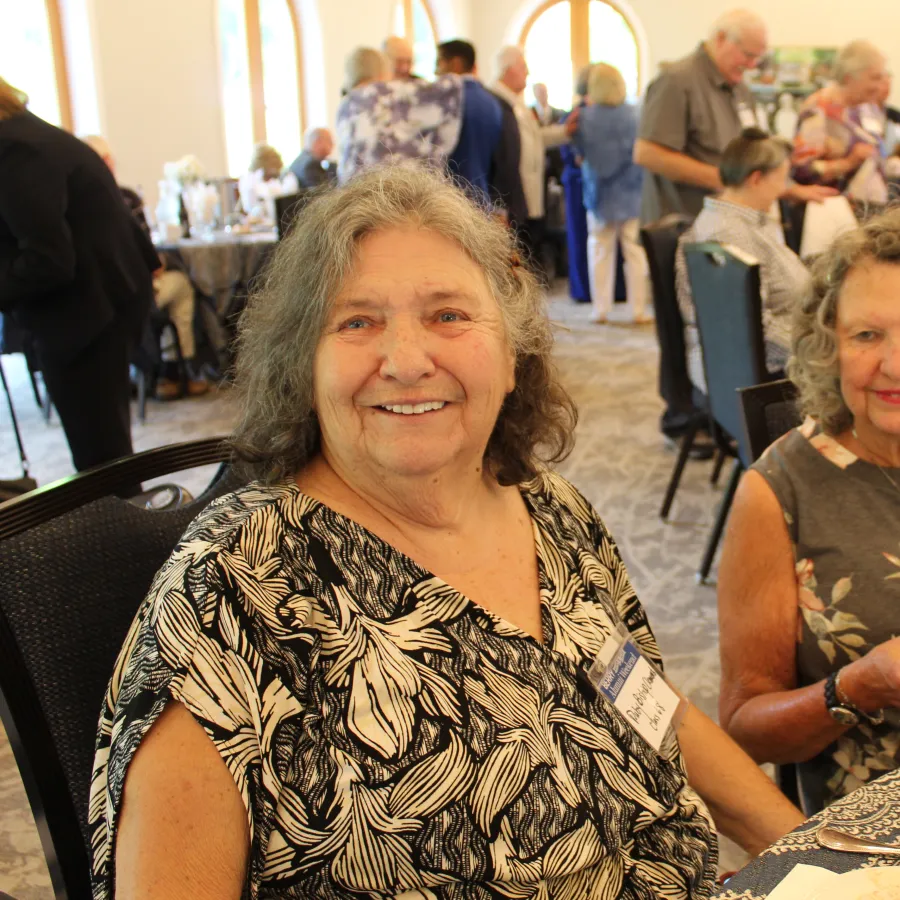 Two elderly women smiling and seated at a table during a social gathering in a banquet hall.