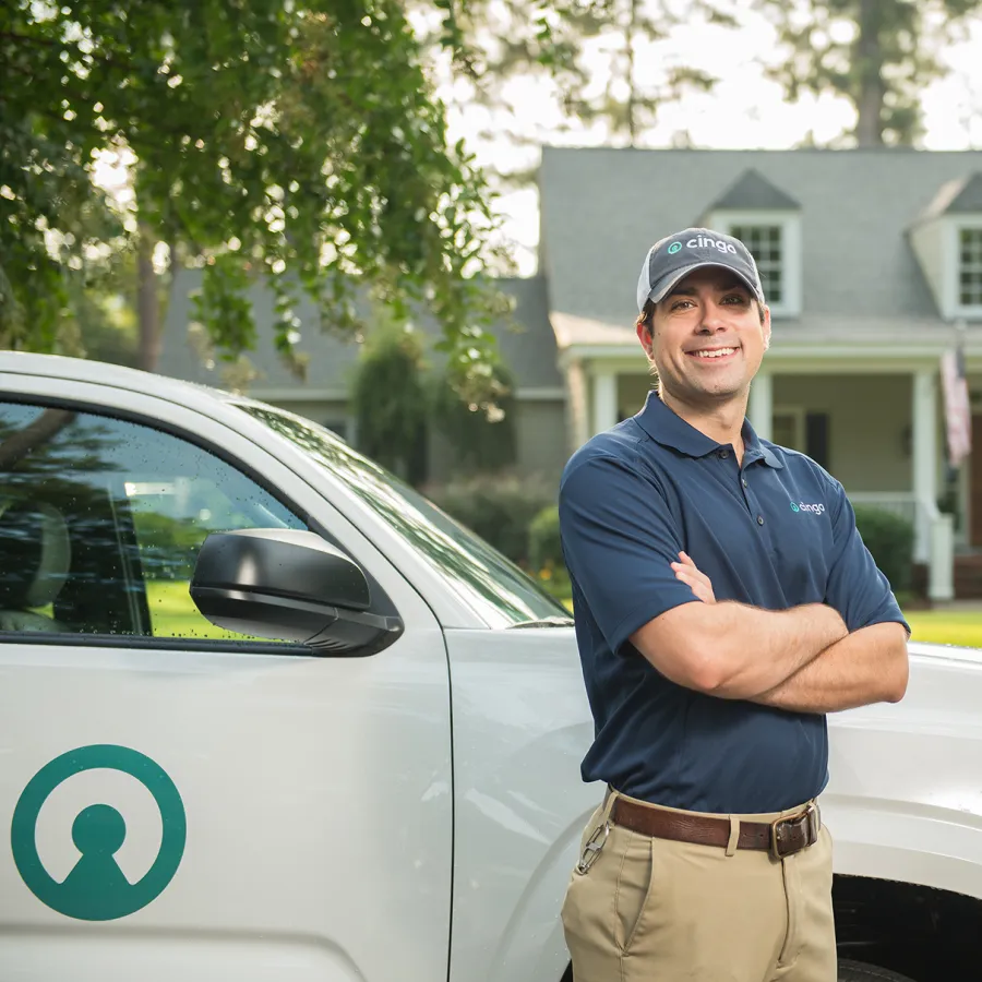 Smiling service professional in uniform stands beside company vehicle with house in background on sunny day