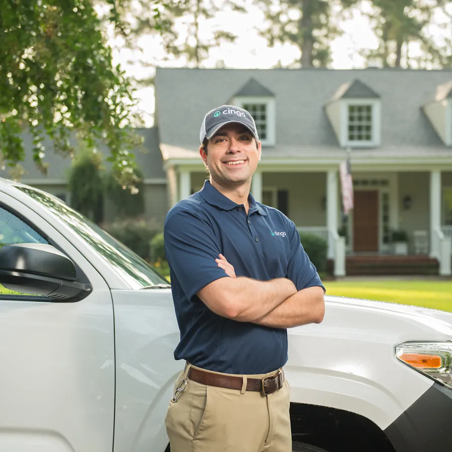 Smiling service professional in uniform stands beside company vehicle with house in background on sunny day