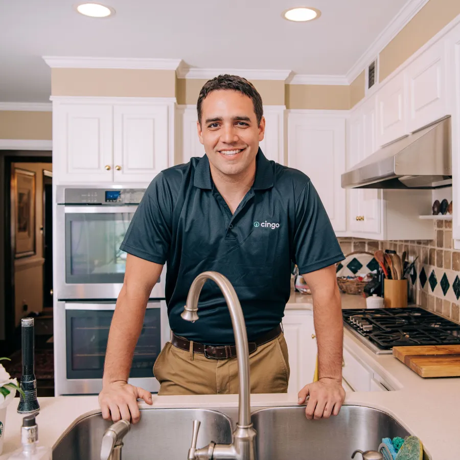 Smiling man in navy polo shirt leaning on kitchen sink with white cabinets and modern appliances in background