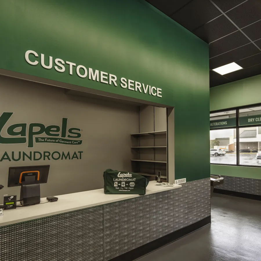 Customer service counter inside Lapels Laundromat with branded wall, computer, and green interior walls.