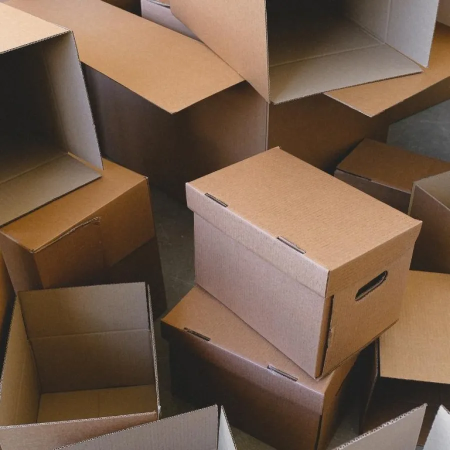 A group of open and closed brown cardboard boxes stacked indoors on a gray floor.