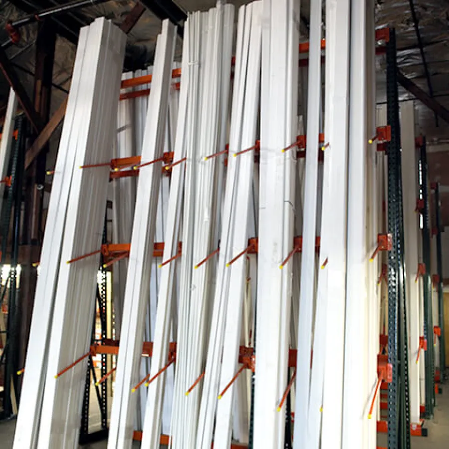 Stacks of white wooden trim pieces stored vertically on orange racks in a warehouse with industrial ceiling.