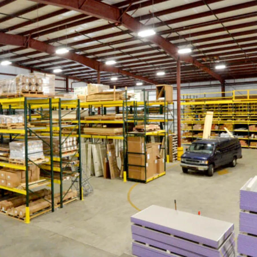 Spacious warehouse with tall shelves stocked with building materials and a black van parked inside under bright lighting.