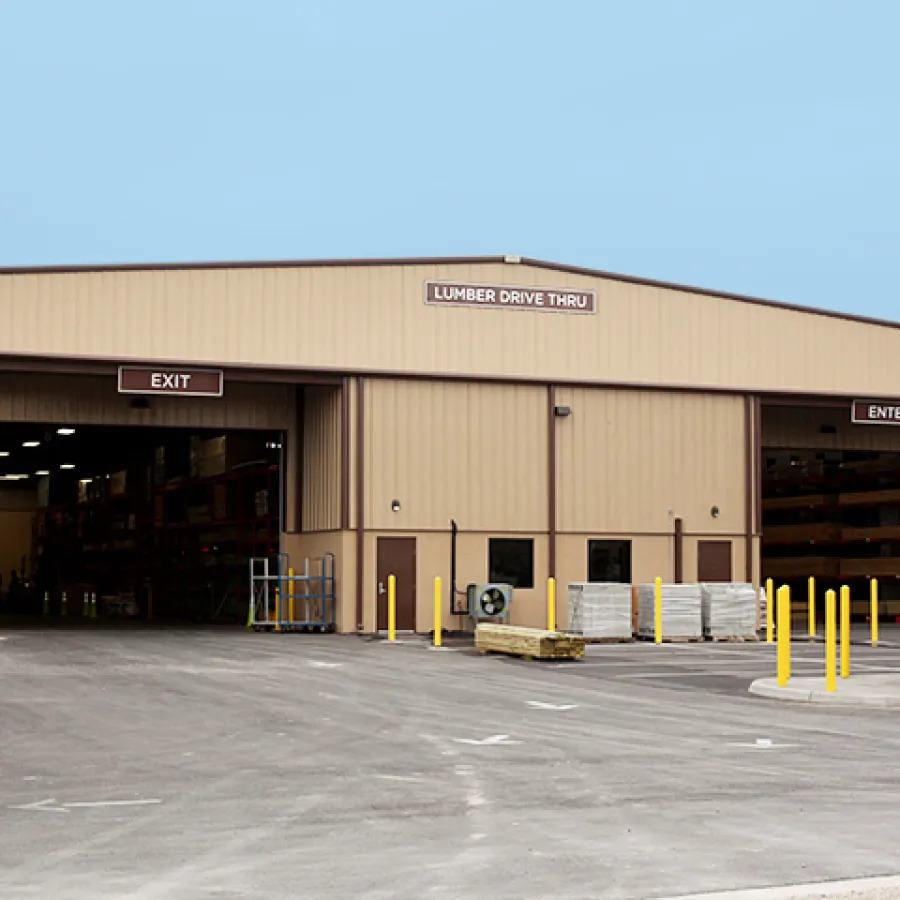 Exterior view of a lumber drive-thru with designated enter and exit bays and stacks of wood inside.