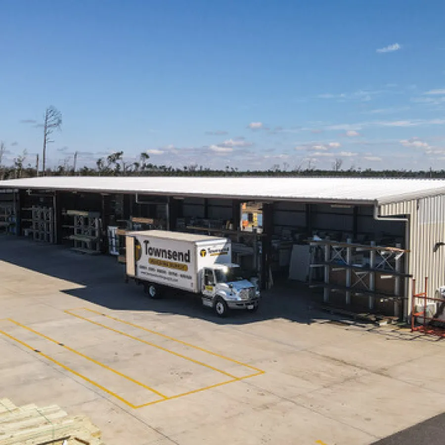 Warehouse with a Townsend delivery truck parked outside under a clear blue sky, surrounded by building materials.