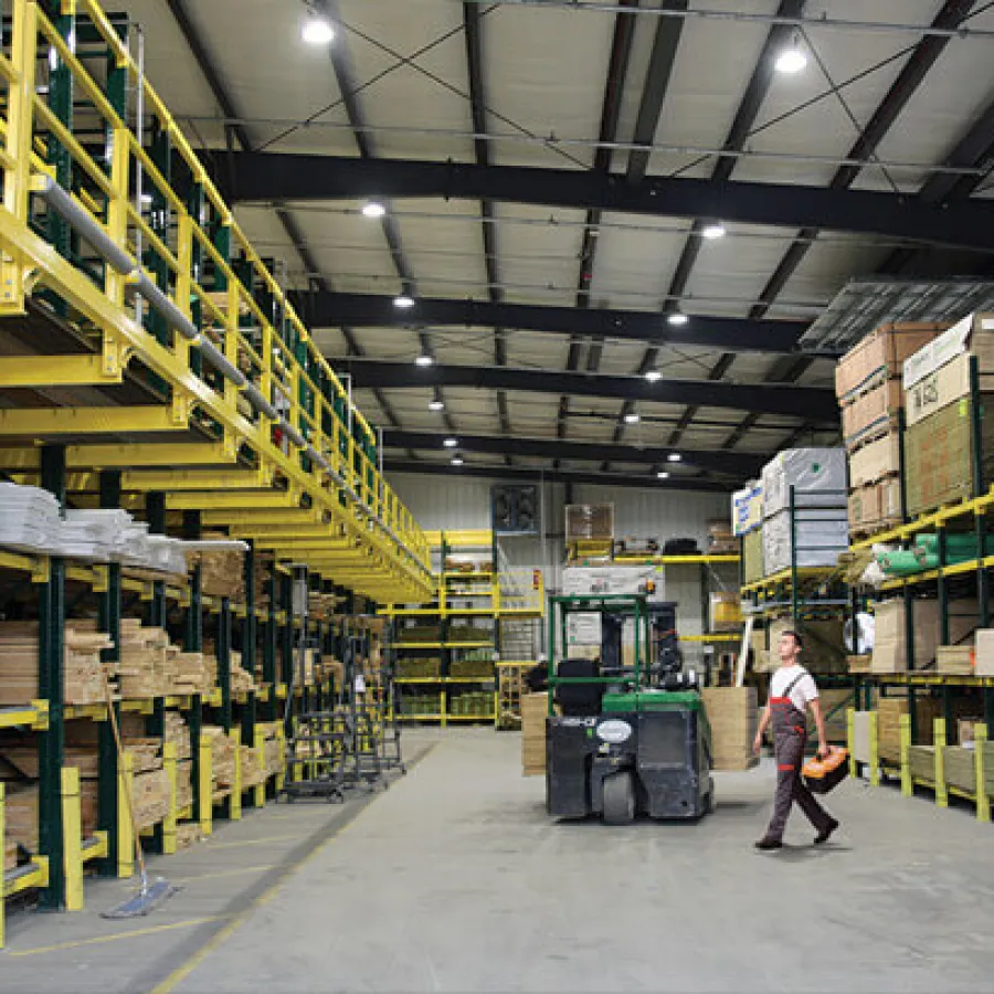 Spacious warehouse with organized shelves of lumber and a forklift operator walking across the floor