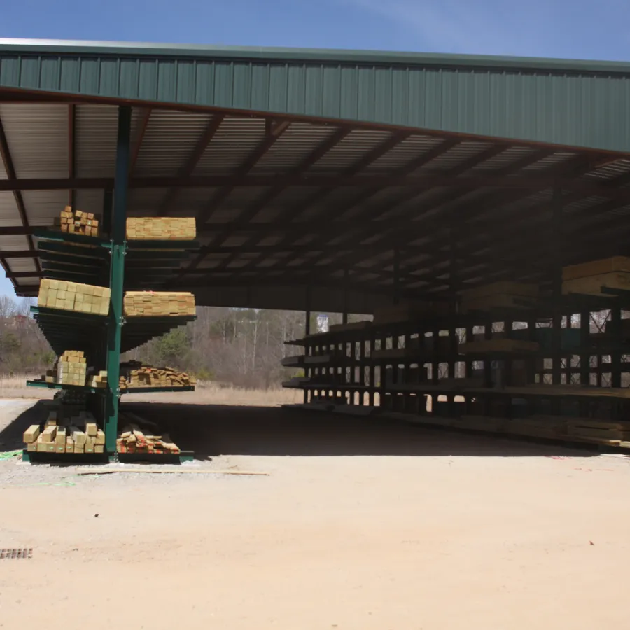 Large open lumber storage shed with stacked wood planks under a metal roof on a clear day