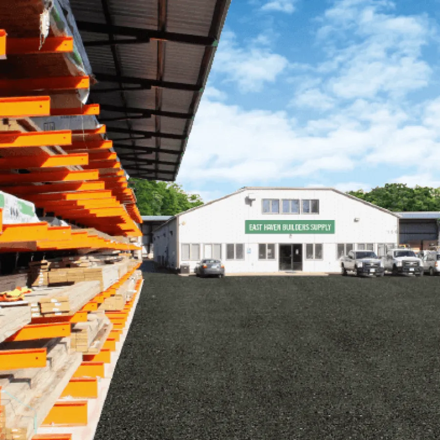 Outdoor lumber yard with stacks of wood on orange racks beside a white building labeled East Town Builders Supply.