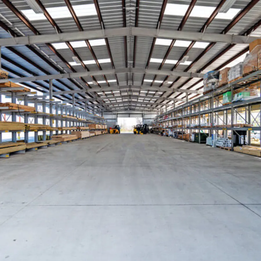 Spacious industrial warehouse with metal shelving stocked with building materials and clear concrete floor.