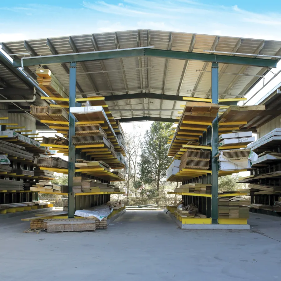 Outdoor lumber storage with wooden planks on metal shelves against clear sky and distant mountains.