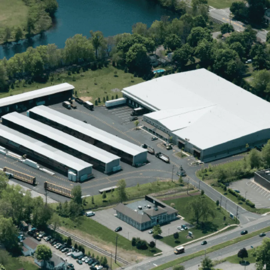 Aerial view of a large warehouse complex with multiple loading docks and parked trailers surrounded by trees and roads.