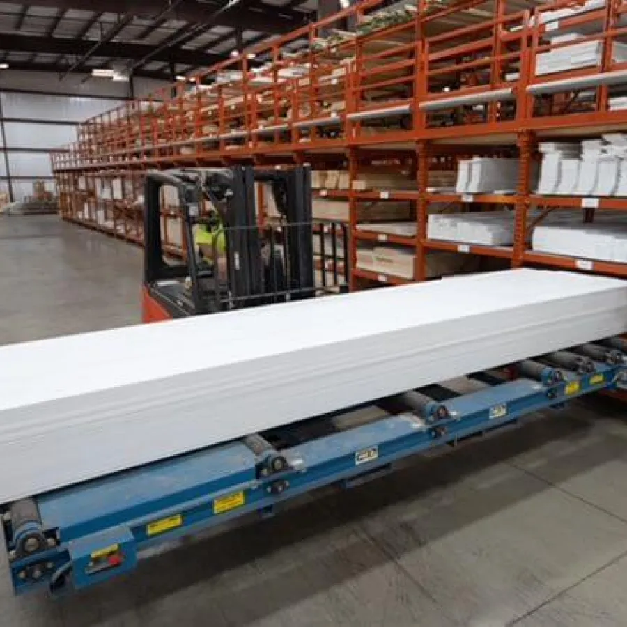 Warehouse scene with forklift carrying long white boards on conveyor, surrounded by metal shelves with supplies.