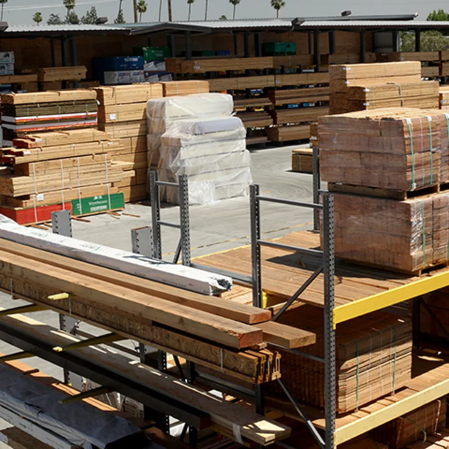Outdoor lumber yard with stacks of wooden planks and beams organized on metal racks under a sunny sky