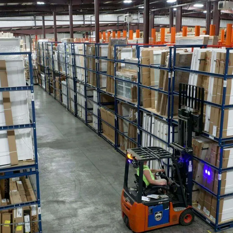 Warehouse interior with tall shelves full of boxes and a worker operating a forklift moving packages.