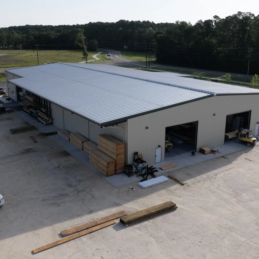 Aerial view of a large industrial warehouse with trucks, forklifts, and stacks of lumber on-site.
