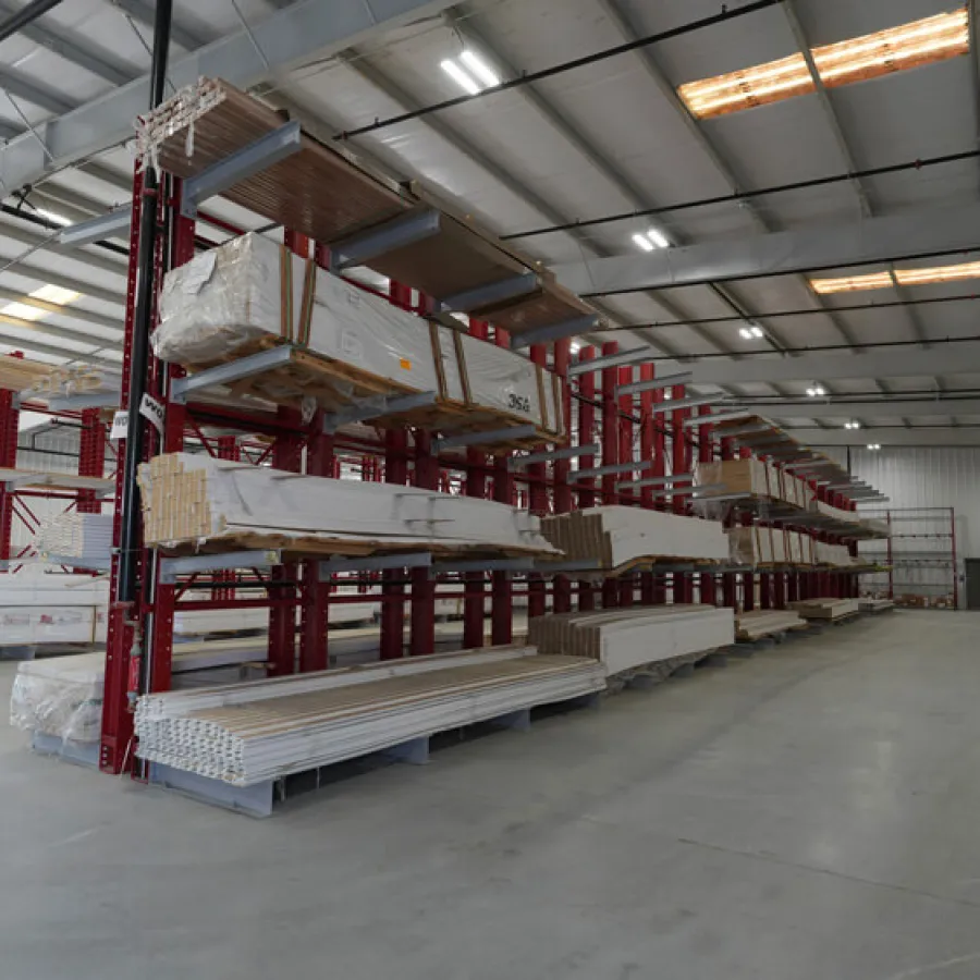 Spacious warehouse interior with red metal racks storing long packaged wood planks and panels.