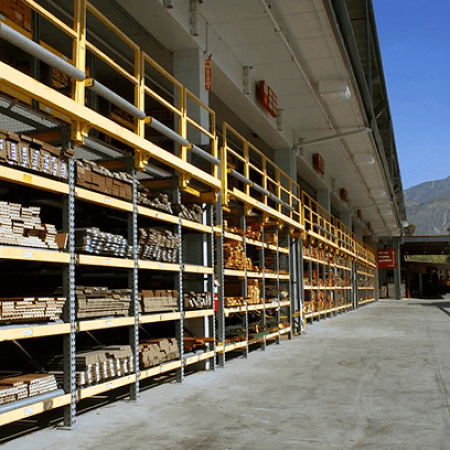 Outdoor lumber storage with wooden planks on metal shelves against clear sky and distant mountains.