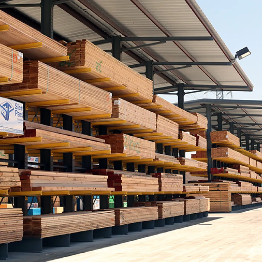 Outdoor lumber yard with stacked wooden planks under metal roofing and clear sky above