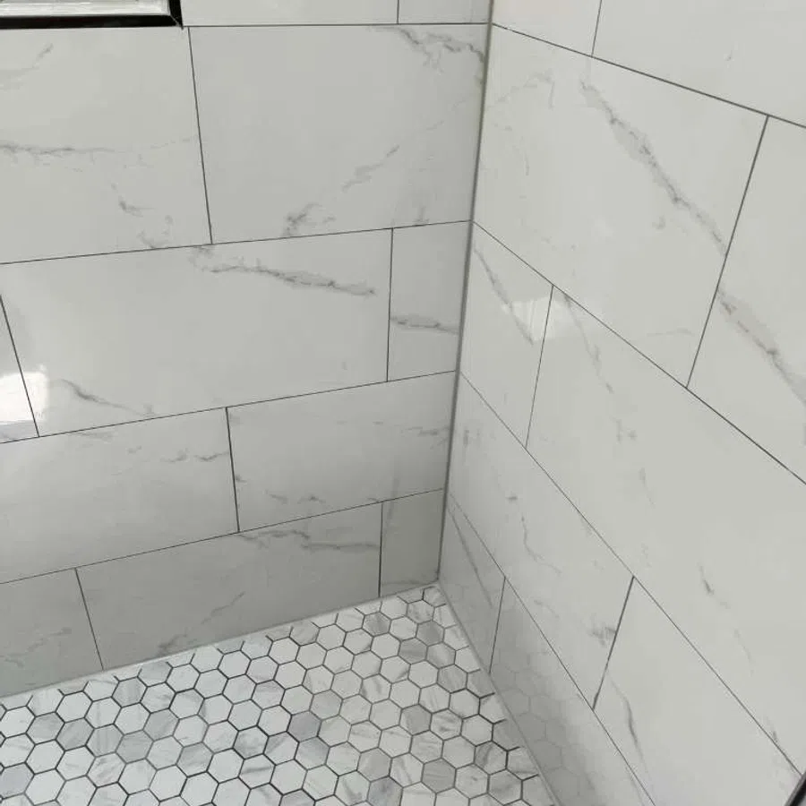 Shower corner with large marble-effect rectangular wall tiles and small hexagonal floor tiles in gray tones.