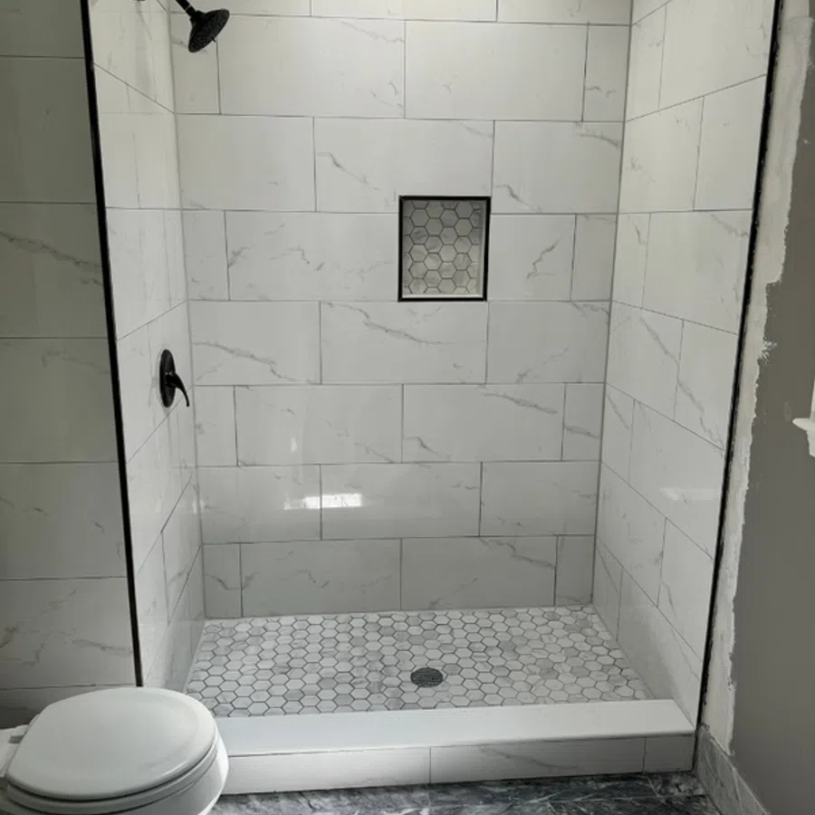 Modern walk-in shower with white marble tiles and hexagon floor tiles next to a white toilet.