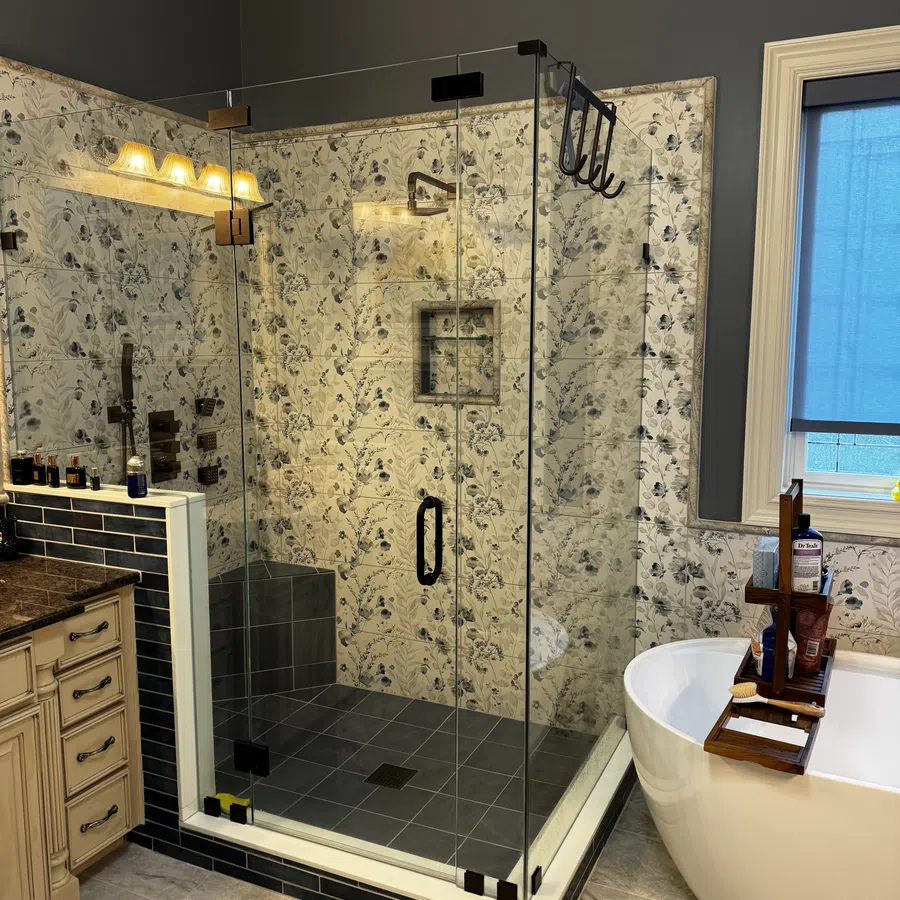 Modern bathroom with glass shower, floral tile walls, freestanding tub with wooden tray, and dark blue accents.