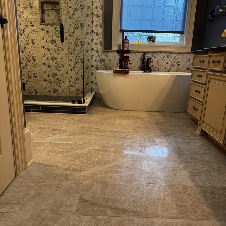 Modern bathroom with freestanding tub, glass shower, floral tile walls, wooden cabinets, and blue window shade.