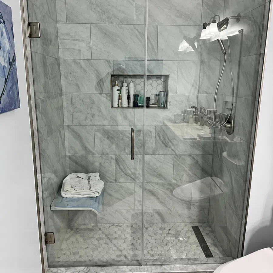 Modern bathroom shower with glass door, marble tiles, built-in shelf, and folded towels on bench.