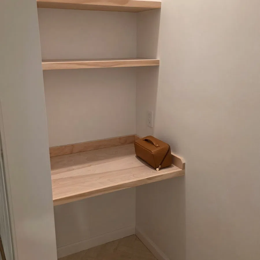 Small corner workspace with two wooden shelves and a wooden desk holding a brown leather bag.