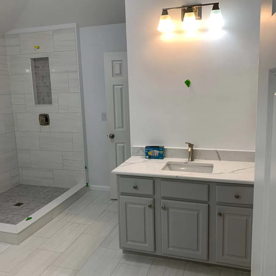 Modern bathroom with gray vanity, white countertop, built-in shower with tiled walls and floor, and overhead lighting.