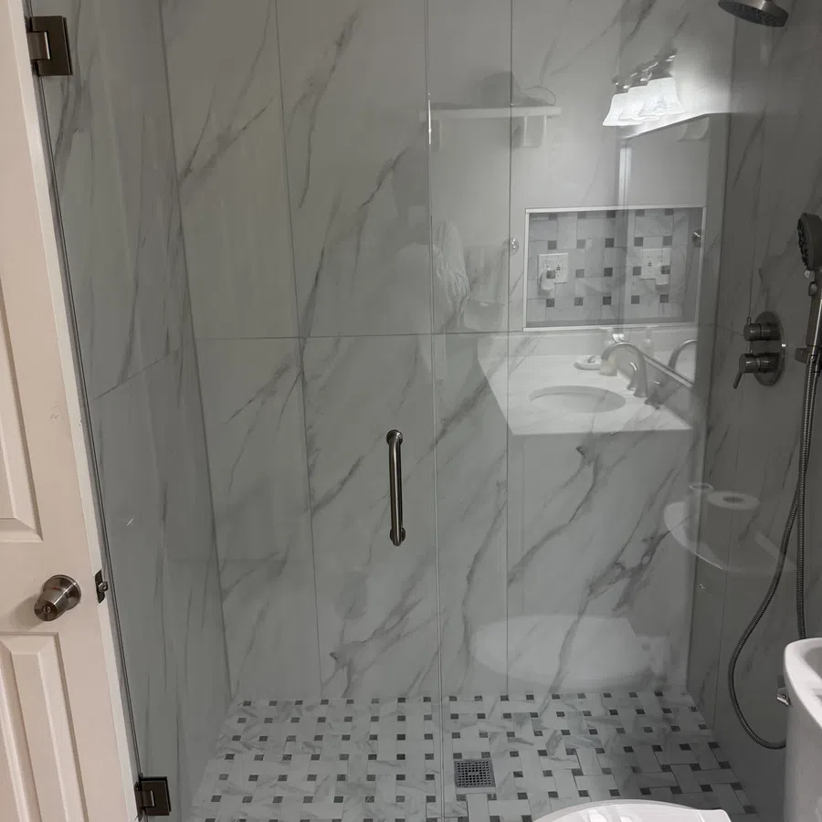 Modern bathroom with marble walls, a glass shower enclosure, tiled floor, and a white toilet.