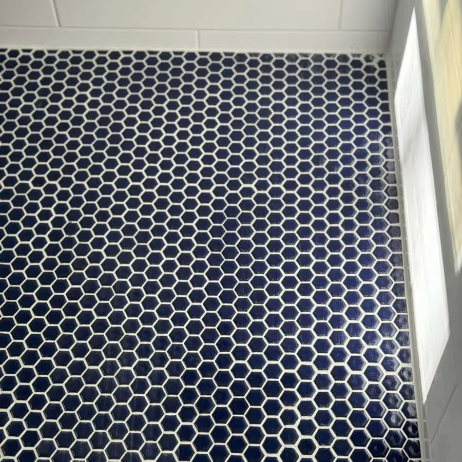 Dark blue hexagonal floor tiles with white grout in a modern bathroom corner with white wall tiles.