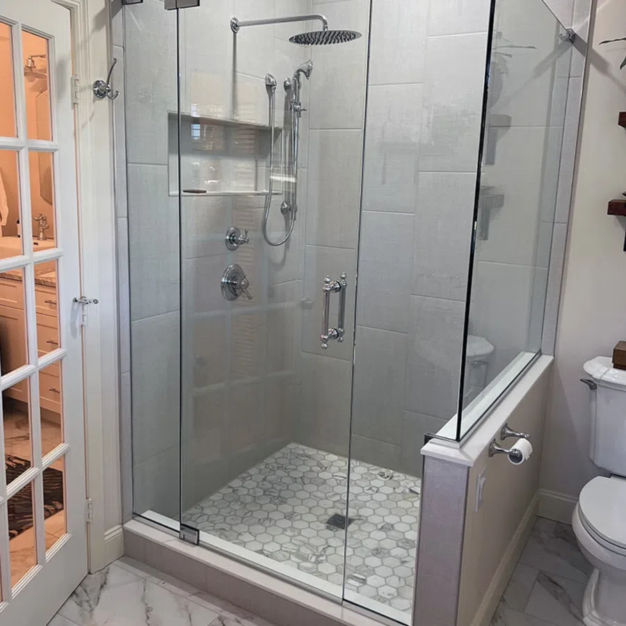 Modern glass shower enclosure with hexagonal tile floor and rain showerhead in a bright bathroom