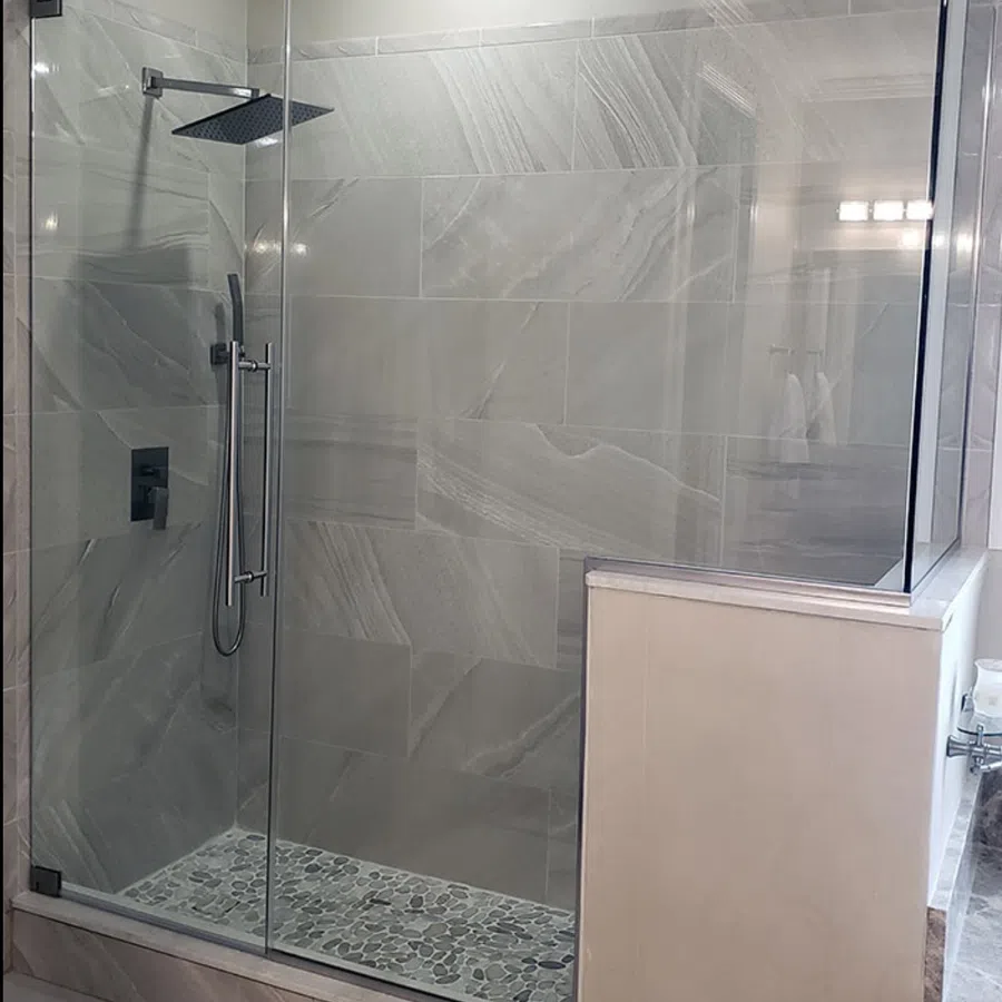 Modern walk-in shower with glass enclosure, gray marble tiles, pebble stone floor, and rain showerhead.