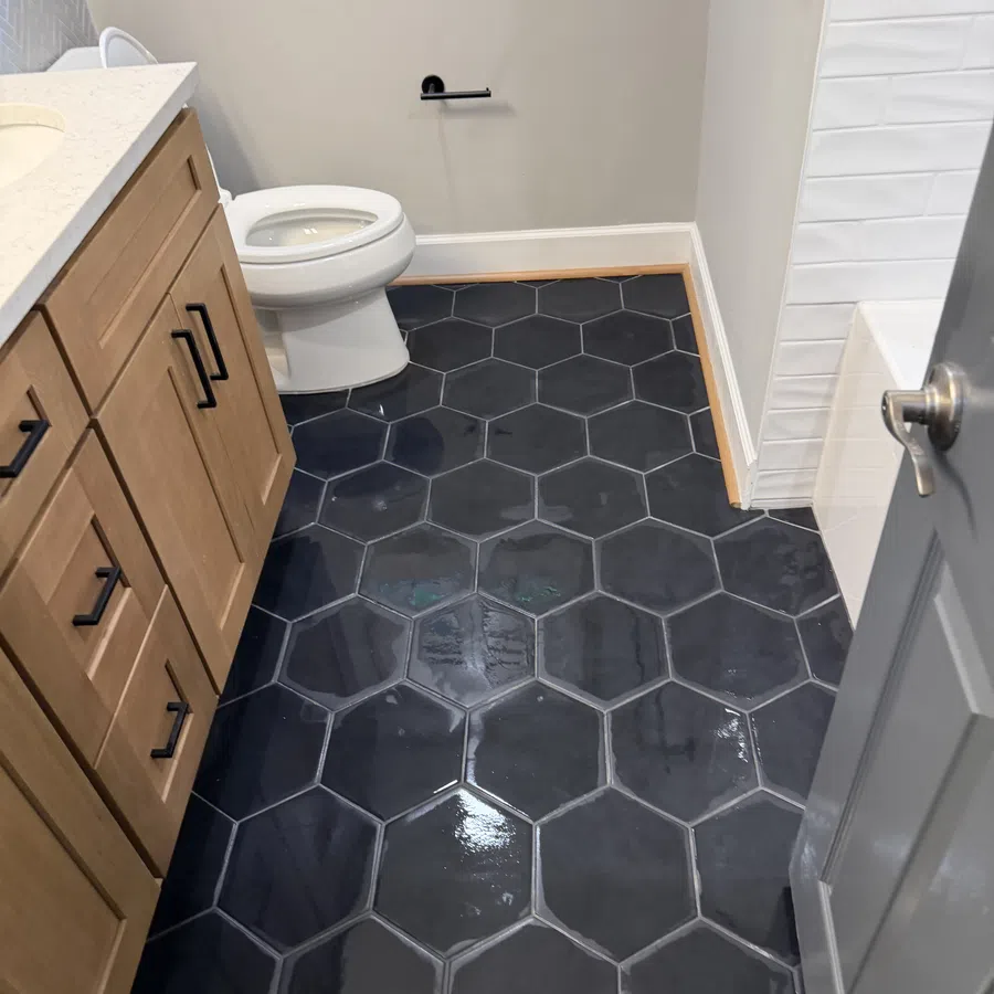 Bathroom floor with large glossy black hexagonal tiles next to a wooden vanity and white toilet.