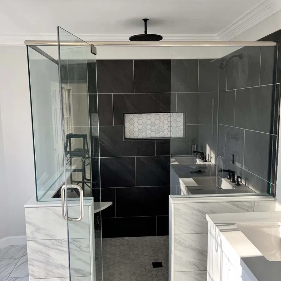 Modern walk-in shower with glass door, black tile walls, hexagonal niche, and marble tile accents in bathroom.