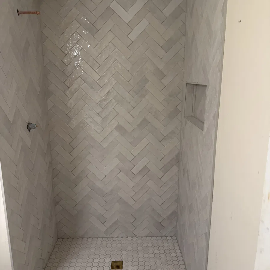 Shower with light grey herringbone wall tiles and round mosaic floor tiles with brass drain cover