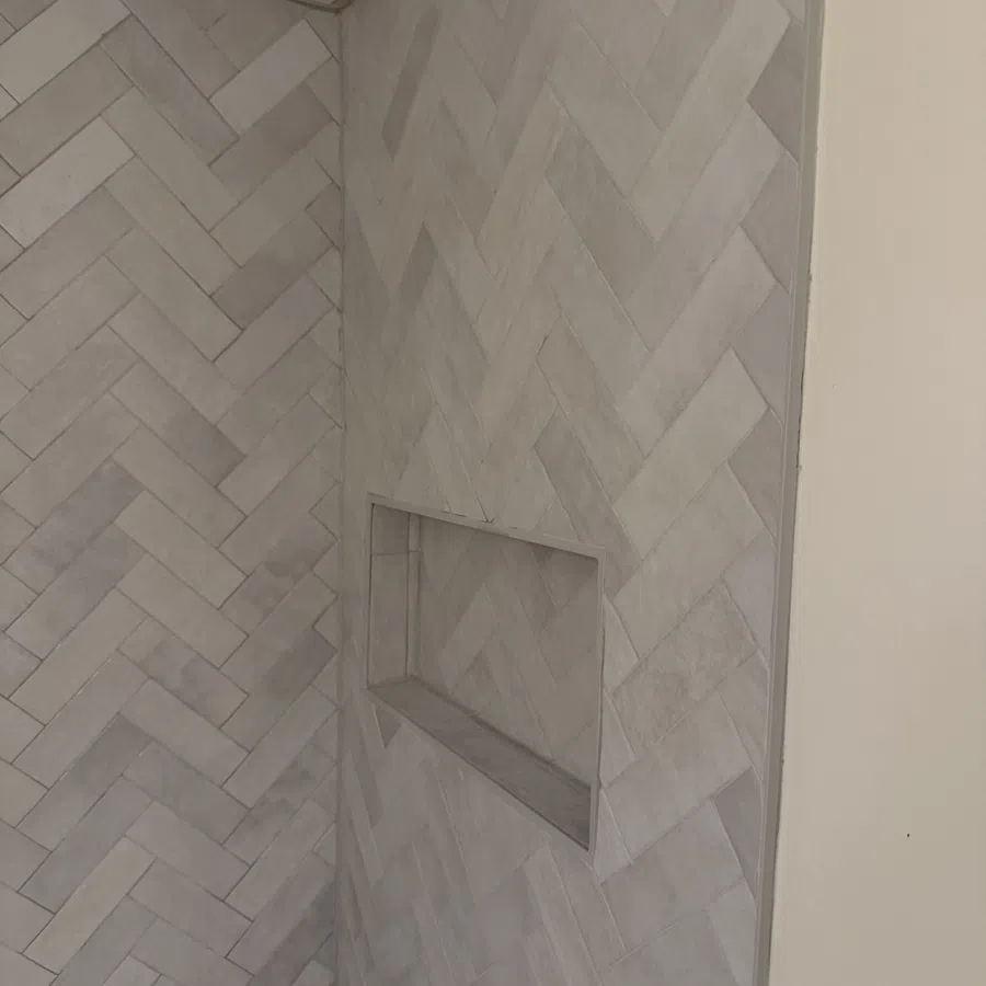Gray herringbone tiled wall with built-in rectangular niche and textured ceiling corner.