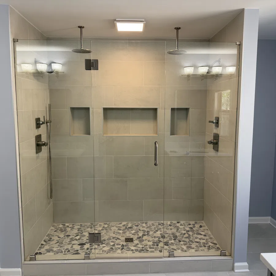 Modern glass walk-in shower with dual rain showerheads and pebble stone tile flooring in grey bathroom.