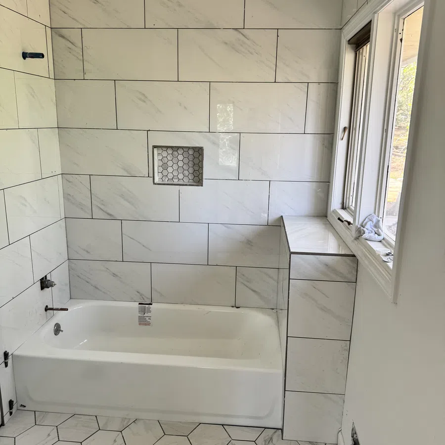 Modern bathroom with white marble wall tiles, hexagonal floor tiles, built-in bathtub, and window natural light.