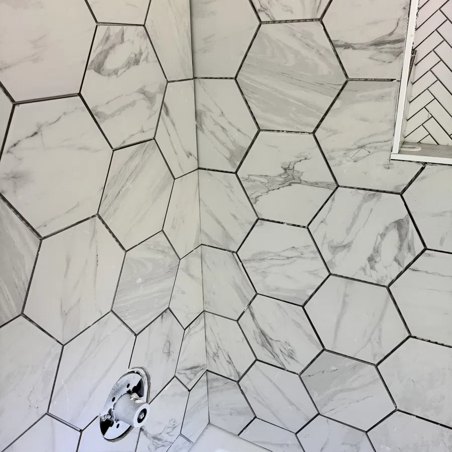 Hexagonal marble-patterned tiles covering bathroom walls around a bathtub with plumbing fixtures in progress.