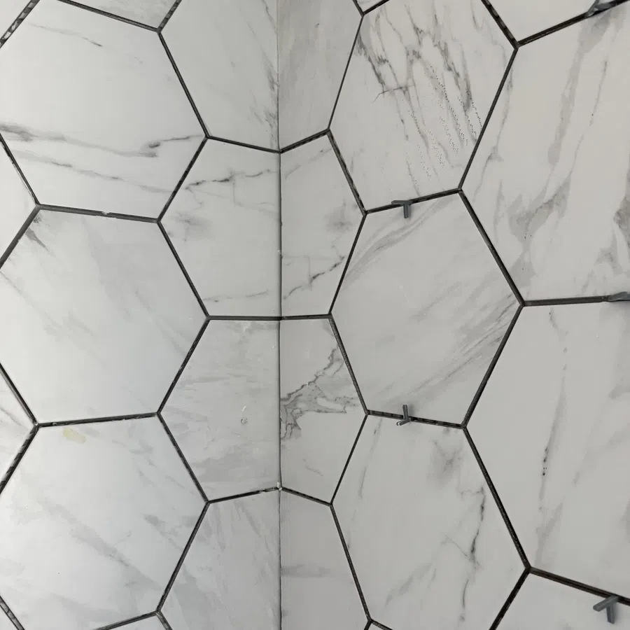 Close-up of marble hexagonal tiles installed on a wall with spacers between grout lines.